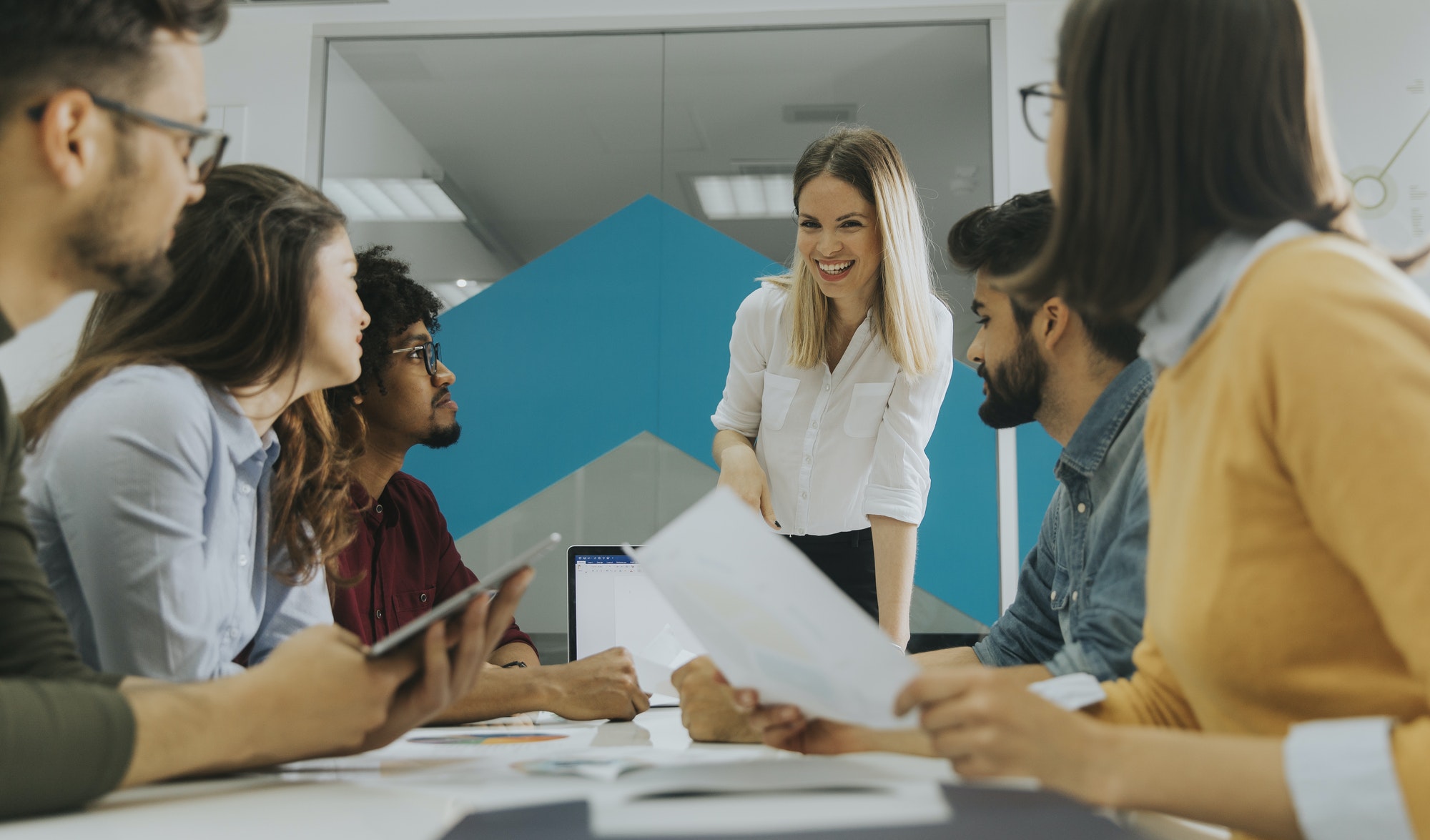 Pretty female team leader talking with mixed race group of people in the office