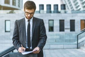 Young businessman standing in a suit and in eyeglasses holds a pen